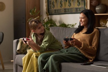 Kadınlar rahat bir oturma odasında kanepede oturmuş video oyunu oynamaktan zevk alıyorlar. Bir kontrolör gülerken, diğeri meşgul.