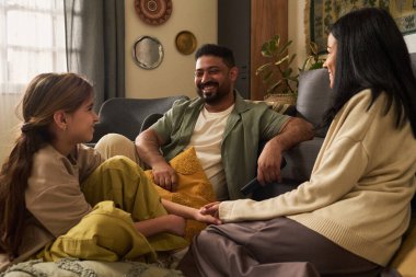Aile bireyleri sıcak oturma odasında birlikte oturuyor, gülüşlerini ve sohbetlerini paylaşıyor, rahat atmosferlerini aydınlatıyorlar.