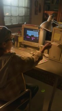 Çocuğun disketi bilgisayara yerleştirip ekranda piksel karakterlerle retro video oyunu oynarken dikey omuz üstü görüntüsü
