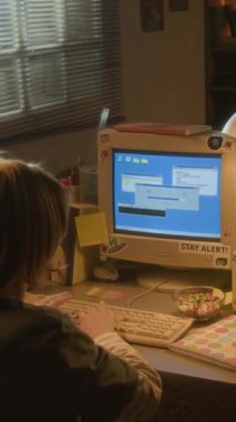 Sarışın bir gencin evde retro bilgisayar kullandığı dikey çekim. Klavyede 90 'lar ayarlı ve daktilo kullanıyor.