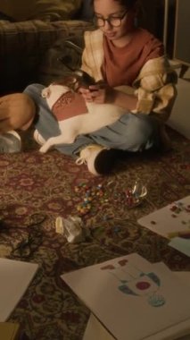 Halıda birlikte oturan iki gencin dikey çekimi. Etrafı çizimler ve ses kasetleriyle çevrili.