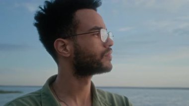 Yüzü asık genç Afrikalı Afrikalı Amerikalı bir adamın deniz kıyısında durup önemli bir karar verirken ya da ikilemi düşünürken yüzünü çevirmesi.