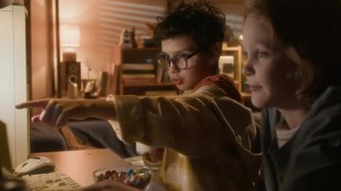 90 'lı yıllarda bilgisayar kullanarak arkadaşlarıyla oyun oynarken kalın gözlükler takan ve soda içen hoş bir çocuğun yan görüntüsü.