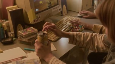 Genç bir çocuğun, arkadaşlarıyla karışık 90 'lar tarzında video oyunları oynarken kola kutusu açtığı yakın plan çekimler.