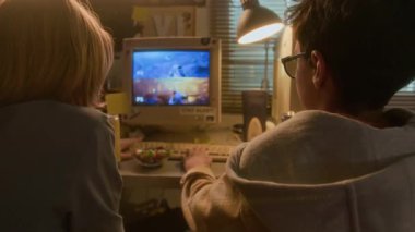 90 'ların çocukluk ortamında geçmişe dönük bilgisayar kullanırken birlikte video oyunu oynayan ve beşlik çakan iki gencin omuz üstü çekimi.