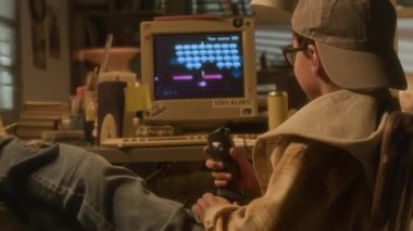 Genç çocuğun oyun oynarken, oyun çubuğu ve retro bilgisayarı kullanırken, masa başında dinlenirken yakın plan çekimini yap.