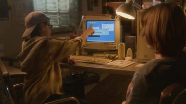 90 'ların ev ortamında arkadaşıyla retro bilgisayar kullanan ve işlevleri açıklayan program etiketlerine işaret eden genç bir çocuğun yan görünüm görüntüsü