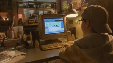 Evde eski bilgisayar kullanıp eğlenirken 90 'lı yaşlardaki genç bir çocuğun fotoğraflarına odaklan.