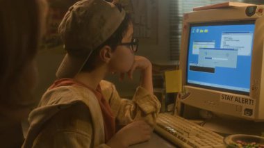 Sıcak tonlu 90 'lı ayarlarda arkadaşlarıyla programları indirirken bilgisayar ekranına bakan çocuğun yan görünümü