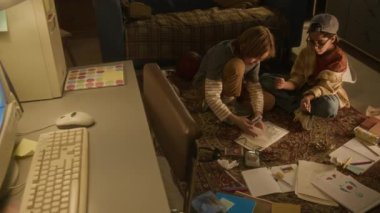 90 'lı yaşlardaki iki çocuk sakız topluyor ve evde otururken onları tahsilat defterine koyuyor.