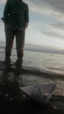 Tanınmayan bir adamın, yaz akşamı gölde durup kağıt teknenin dalgalar üzerinde sallanışını ve sonra da yürüyüp gidişini izlediği dikey tecrit görüntüsü.