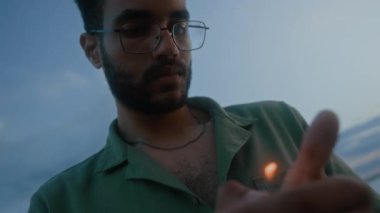 Hollandalı Afro-Amerikalı adamın yüzünün ve ellerinin, elinde çakmak tutarken ve rüzgarda titreyen ateşi izlerken, akşamları dışarıda yalnız başına vakit geçirdiği orta boy yakın çekim.