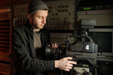 Genç adam TV minibüsünde çekim için ekipman hazırlarken profesyonel video kamerada güç düğmesine basıyor.