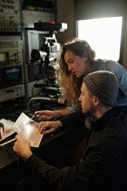 Genç bir kadın, erkek operatörle yayın programı tartışması sırasında belgeye işaret ederek çekim için hazırlanıyor.