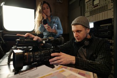 Ciddi bir adam, kadın gazeteciye karşı ses konsoluyla mikrofonu karıştırırken profesyonel video kamerayı açıyor