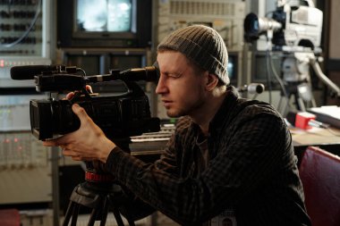 Genç operatör ya da videograf stüdyoda ya da TV minibüsünde çekim için hazırlanırken profesyonel video ekipmanı kullanıyor