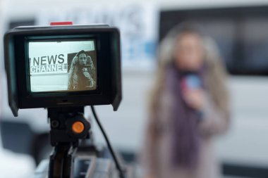 Genç bayan gazetecinin mikrofonla haber kanalının TV minibüsüne karşı konuştuğu profesyonel video kamera ekranı