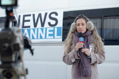 Mikrofonlu genç bir kadın video kameranın önünde duruyor ve röportaj sırasında mevcut durumu anlatıyor.