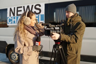 Profesyonel video kameralı genç kendine güvenen erkek operatör TV minibüsü ile kadın gazeteciyle iletişim kuruyor.