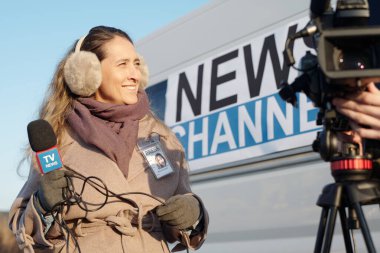 Mikrofonlu gülümseyen genç bayan muhabir kamerayla operatörün önünde kamerayı çekmeye hazırlanıyor.