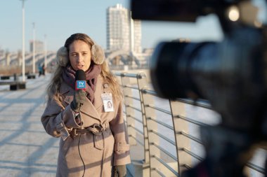 Genç bayan gazeteci son dakika haberi sırasında kamerayla operatörün önünde durarak durumu bildiriyor.