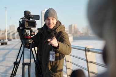 Haberleri çekmeden önce profesyonel video kameranın önünde duran mutlu genç operatör kadın gazeteciyi işaret ediyor.