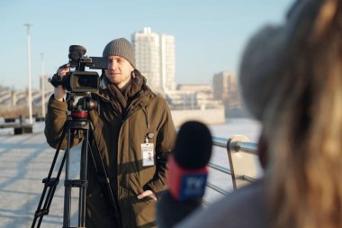 Genç erkek operatör ya da videografın haber çekerken kadın gazeteciyi mikrofonla vurmasına odaklan