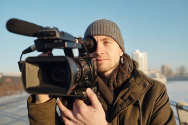 Erkek operatör ya da kameraman kentsel ortamda dururken video kameraya yeni görüntüler ya da görüntüler çekiyor