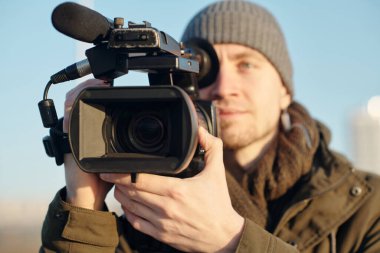 Yeni açık hava çekimlerine hazırlanırken video kamerayı ayarlayan genç erkek kameramanın eline odaklan