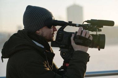 Günlük kıyafet çekimi videosundaki operatörün yan görüntüsü veya kentsel çevredeki profesyonel kamerada röportajı