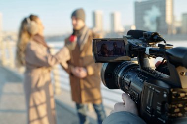 TV kanalının açık hava röportajı sırasında ekranda iletişim kuran genç bir adam ve kadınla video kameraya odaklan.