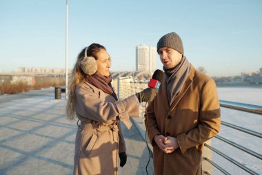 Mikrofonlu genç gazeteci şehir ortamında televizyon kanalı için röportaj yaparken erkek politikacıya bakıyor