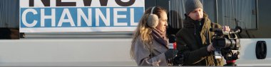 Erkek operatörün yanında duran ve haber çekmeden önce profesyonel video kamerayı ayarlayan genç kadın gazetecinin lideri