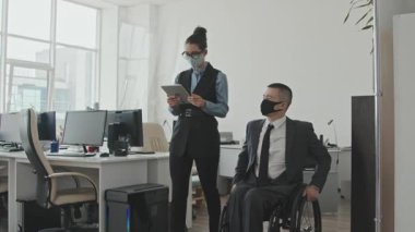 Yüz maskeli bir iş kadınının elinde tabletle iş adamının yanında yürürken konuşmasının yavaşlığını izlemek.