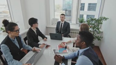 Tekerlekli sandalyedeki erkek CEO 'nun toplantı odasında otururken ve resmi kıyafet giyen iş arkadaşlarıyla iş konuşurken yüksek açılı görüntüsü.