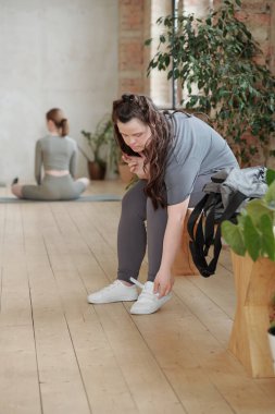 Spor kıyafetli bir kızı spor ayakkabılarını giyerken spor salonunda yedek kulübesinde otururken sakatla.