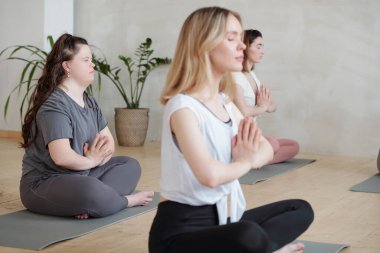 Birkaç genç bayan spor salonunda yerde yoga yapıyor.