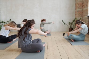Aktif giysili kızlar yoga antrenmanında kollarını önlerine uzatırlar.