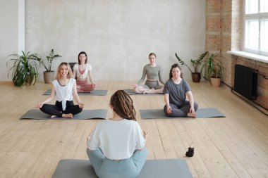 Bir grup kız hasırlar üzerinde egzersiz yaparken yoga eğitmenine bakıyor.