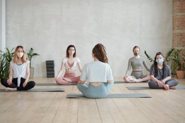 Maskeli kızlar, yoga dersinin başında antrenör dinleyip yeni egzersizleri anlatıyor.