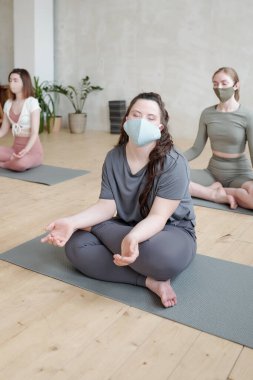 Yoga yaparken koruyucu maskeli kız minder üzerinde rahatlama egzersizi yapıyor.