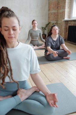 Kadın eğitmen ve iki genç kadın jimnastik salonunda yoga yapıyorlar.