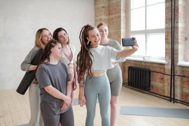 Akıllı telefonuyla spor salonunda grubuyla selfie çeken mutlu genç bayan antrenör.