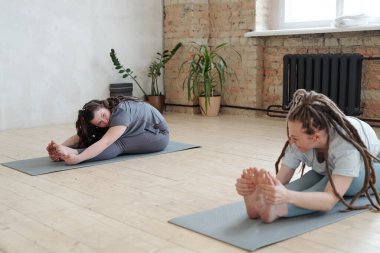 Genç antrenör, engelli kıza yoga yaparken esneme egzersizi yapmayı gösteriyor.