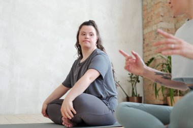 Spor yaparken yoga eğitmenine bakan ve onu dinleyen aktif kıyafetli ciddi bir kadın.