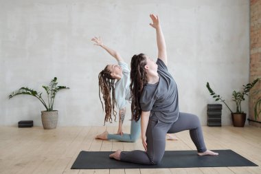 Aktif giyimli küçük bir grup genç bayan minderler üzerinde yoga egzersizi yapıyor.