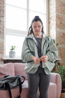 Spor kıyafetli esmer kadın spor salonuna giderken oturma odasındaki kanepenin önünde duruyor.