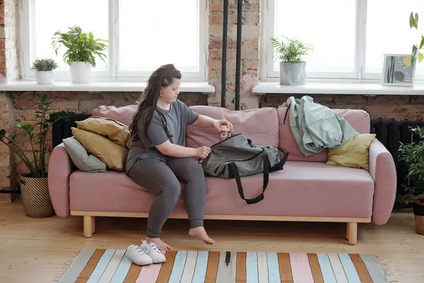 Genç sakat kadın koltukta otururken spor çantasına su koyuyor.