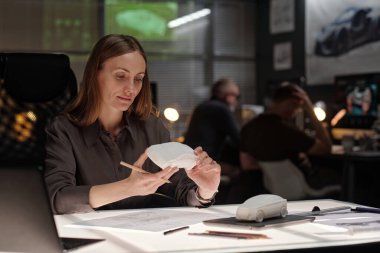 Otomotiv geliştirme bürosunda çalışırken elindeki beyaz araba modeline bakan genç bir kadın mühendis.