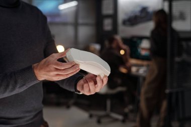 Uzun kollu kazak giyen yetişkin erkek mühendisin elleri beyaz araba modelini tutarken yeni aracın özelliklerini inceliyor.